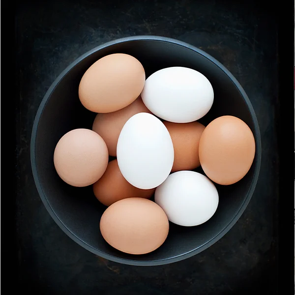 Top-down view of a bowl filled with brown and white eggs on a dark surface.