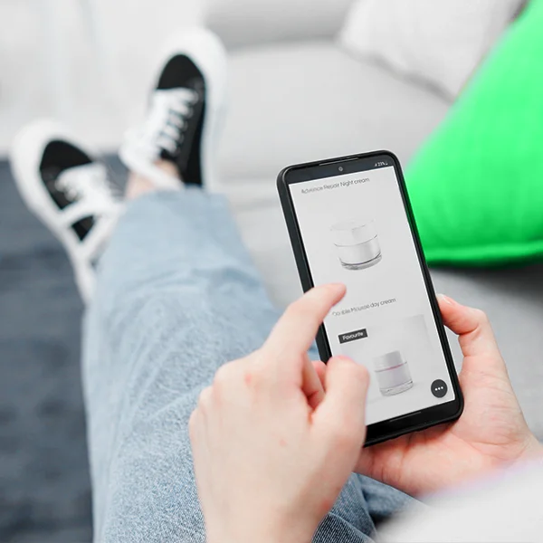 A person reclines on a couch while using a smartphone to browse skincare products on an online shopping app.