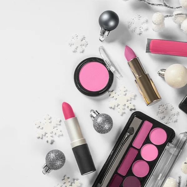 Flat lay of makeup products—including lipsticks, mascara, blush, and an eyeshadow palette—arranged on a white surface with holiday decorations.