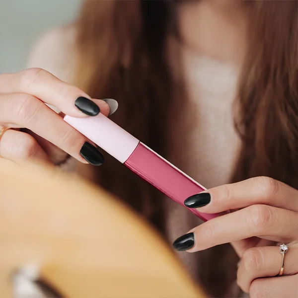 A person holds a tube of pink liquid lipstick, showing it close to a mirror.