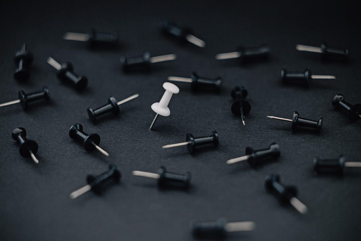 Push pins scattered on a dark surface with one white pin standing out, representing testing, learning, and identifying what works.