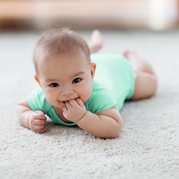 A baby lies on a soft carpet, smiling.