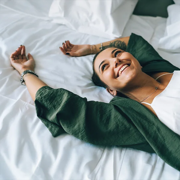 A woman lies on a bed with her arms stretched out, smiling contentedly.