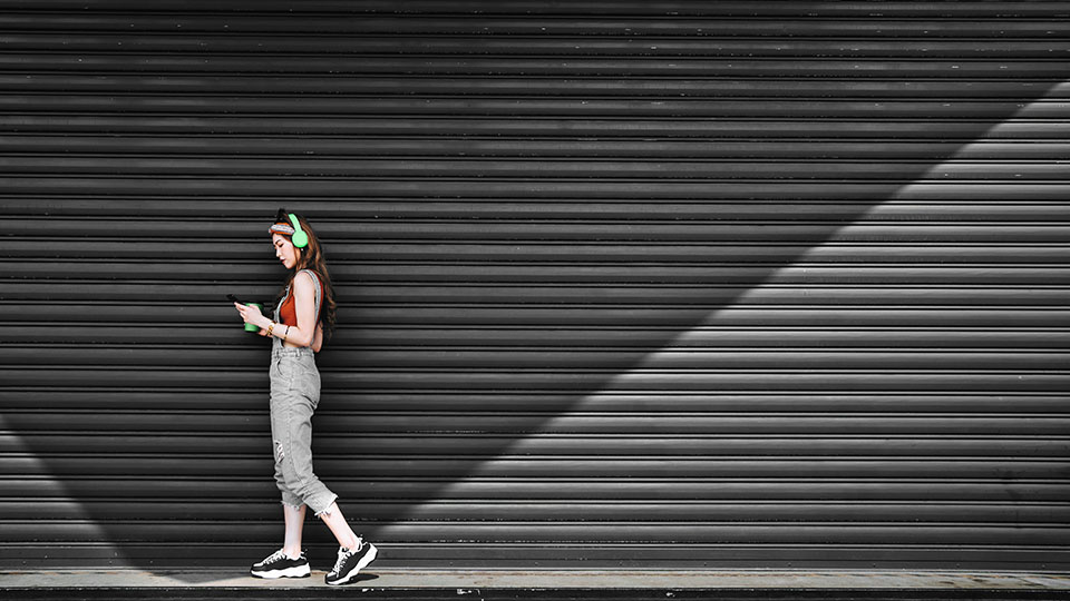 A Woman walking and looking at their cellphone with green headphones on