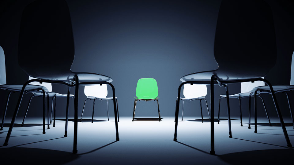 A green chair at the center of a ring of neutral chairs.