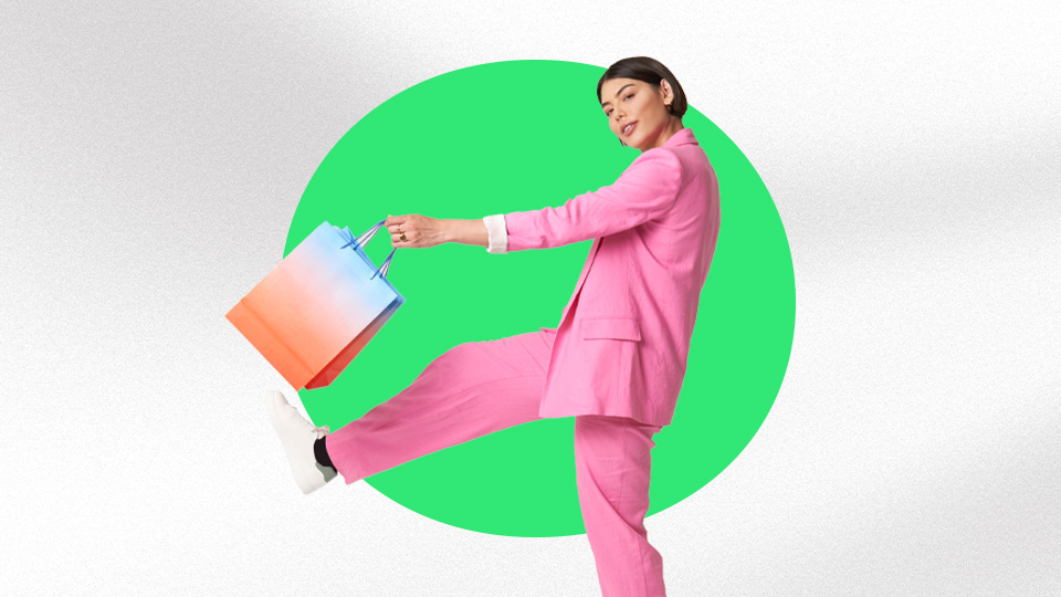 A woman wearing a pink suit and kicking a blue and orange shopping bag.