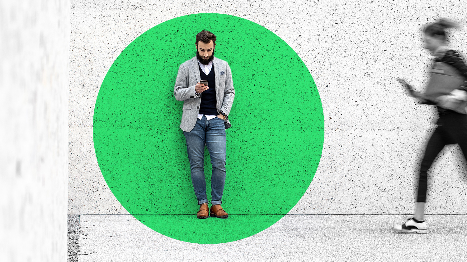 A man leaning on a wall and looking at their cell phone.