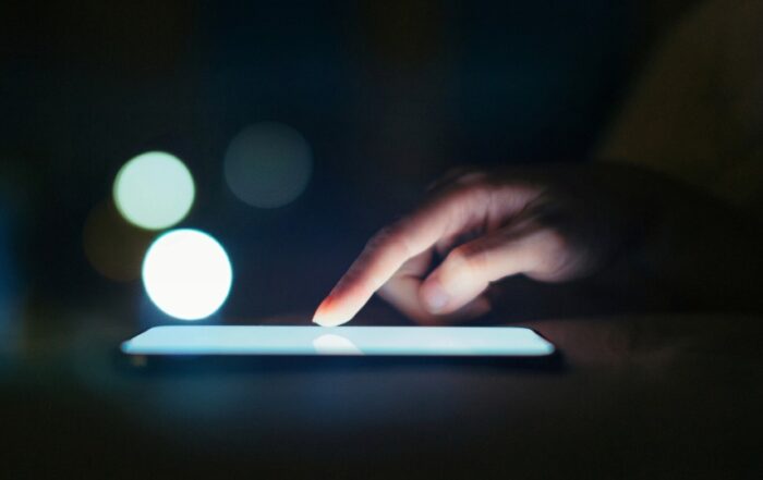 A finger scrolling on a cell phone in a dark room.