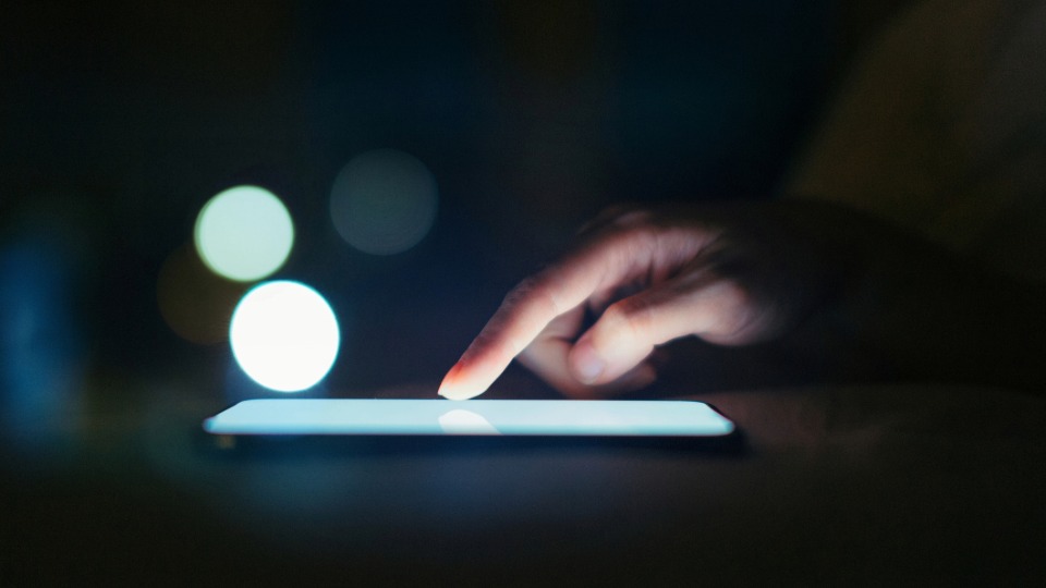A finger scrolling on a cell phone in a dark room.