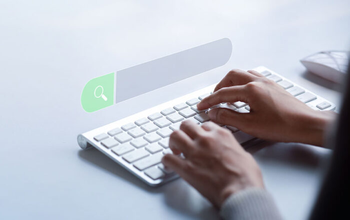 A pair of hands typing on a keyboard with a search bar suspended above the keyboard.