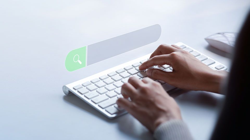 A pair of hands typing on a keyboard with a search bar suspended above the keyboard.
