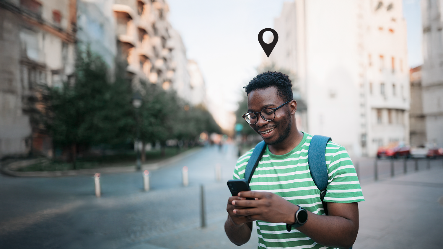 A man smiling and looking at their phone while on a walk. A location pin is above their head. A man smiling and looking at their phone while on a walk. A location pin is above their head.
