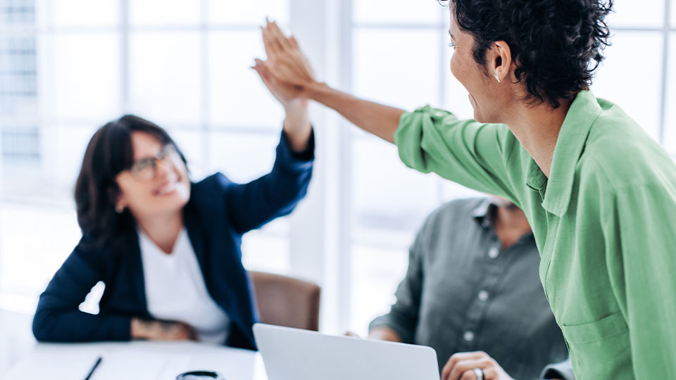 Two colleagues sharing a high five during a work meeting. Two colleagues sharing a high five during a work meeting.
