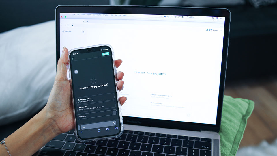 Someone holding their cell phone with the ChatGPT interface on the screen, while also having ChatGPT ready on their laptop screen.