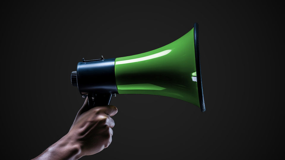 A green megaphone being held by a hand. A green megaphone being held by a hand.