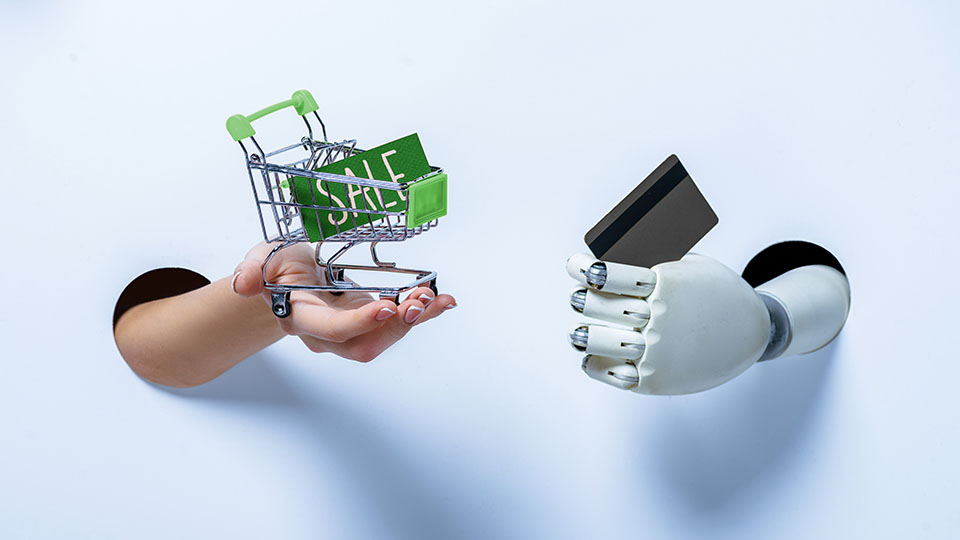 A human hand holding a green shopping cart on the left, and a white robotic hand holding credit card on the right in front of a white background. A human hand holding a green shopping cart on the left, and a white robotic hand holding credit card on the right in front of a white background.
