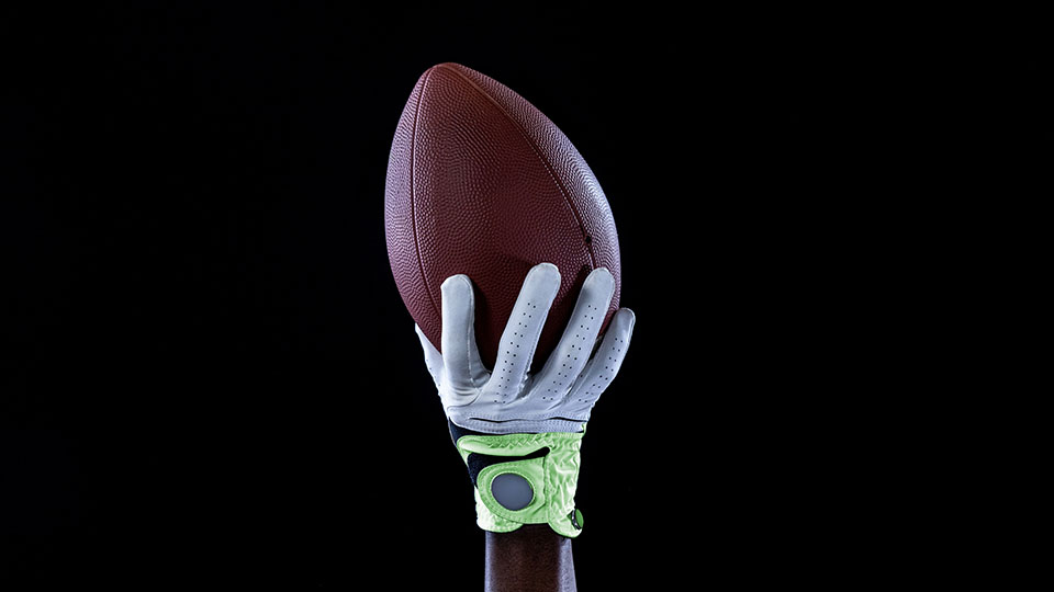 A receiver catching an American football with their gloved right-hand.