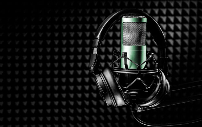 A pair of headphones surrounding a green microphone inside a padded recording studio.