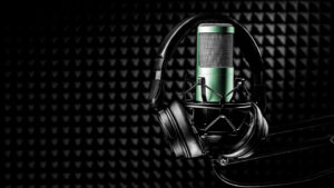 A pair of headphones surrounding a green microphone inside a padded recording studio.