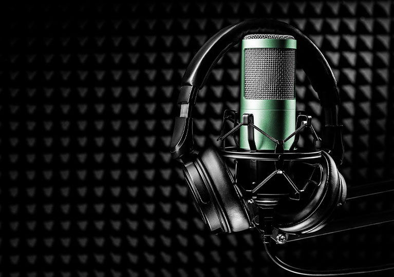 A pair of headphones surrounding a green microphone inside a padded recording studio.