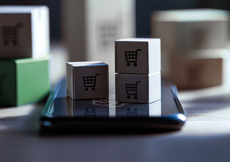 Three small boxes on top of a cell phone. The boxes have shopping cart icons on them.